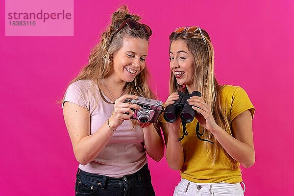 Zwei junge blonde kaukasische Frauen  die sich die Fotos im Urlaub ansehen  vor einem rosa Hintergrund