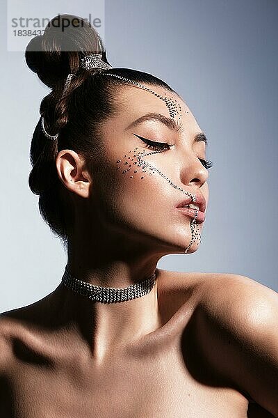 Schöne Frau mit kreativer Frisur und Makeup mit Strasssteinen. Schönes Gesicht. Foto im Studio aufgenommen