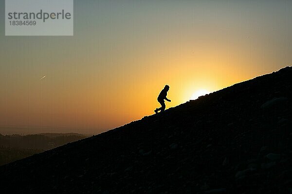 Silhouette eines Mannes klettert auf den Gipfel eines Hügels mit Sonnenuntergang oder Sonnenaufgang Hintergrund. Polen  Polen  Europa