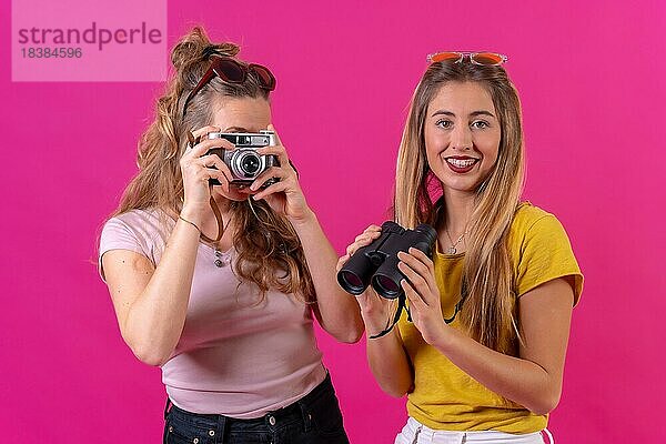 Zwei junge blonde kaukasische Touristen Porträt mit Kamera und Ferngläser  vor einem rosa Hintergrund