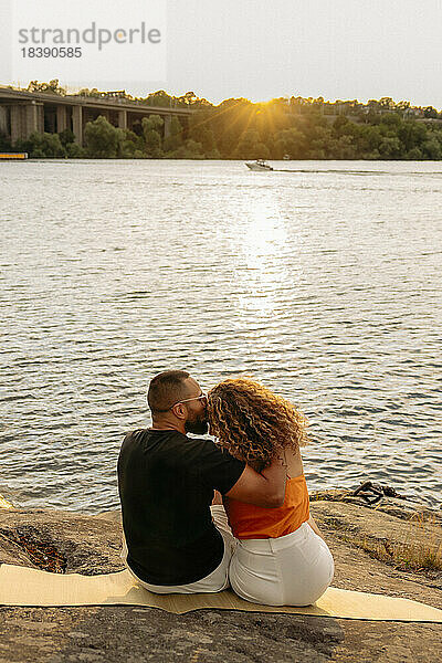 Mann küsst Freundin auf einer Picknickdecke am Meer