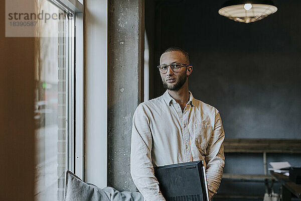 Porträt eines jungen Geschäftsmannes mit Laptop  der in einem Start-up-Unternehmen steht