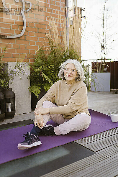 Glückliche ältere Frau sitzt auf einer Übungsmatte auf der Terrasse