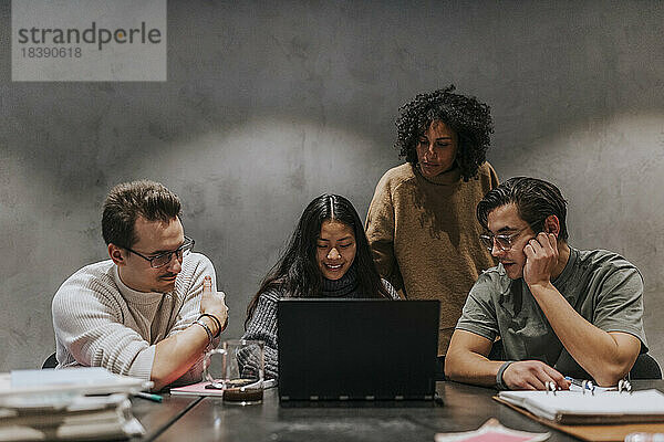 Männliche und weibliche Geschäftskollegen diskutieren über Laptop am Konferenztisch in einem Startup-Unternehmen