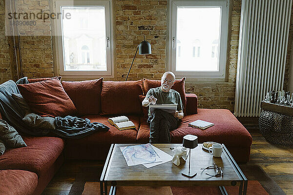 Älterer Mann malt  während er auf dem Sofa im Wohnzimmer zu Hause sitzt