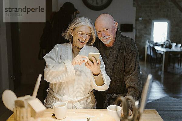 Glückliche ältere Frau teilt Smartphone mit Mann zu Hause