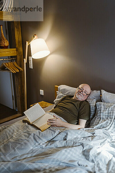 Älterer Mann mit Buch  der ein Nickerchen macht  während er zu Hause auf dem Bett liegt