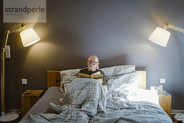 Älterer Mann verbringt seine Freizeit beim Lesen eines Buches auf dem Bett zu Hause