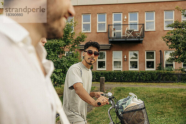 Junger Mann mit Sonnenbrille auf dem Fahrrad  der mit einem Freund spazieren geht