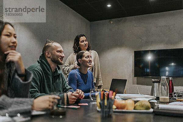 Lächelnde multirassische männliche und weibliche Kollegen während einer Sitzung im Sitzungssaal eines Kreativbüros
