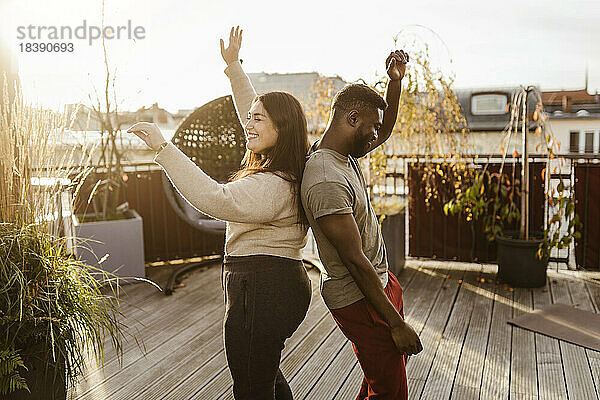 Seitenansicht eines unbekümmerten Paares  das Rücken an Rücken auf einer Terrasse tanzt