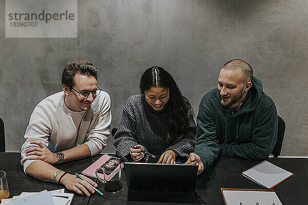 Lächelnde Geschäftsfrau  die mit männlichen Kollegen am Arbeitsplatz eine Strategie am Laptop diskutiert