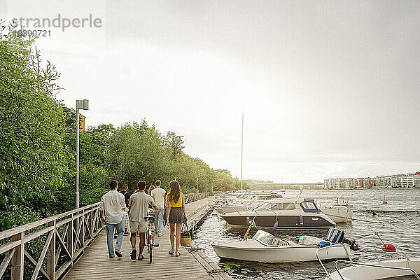 Rückansicht von männlichen und weiblichen Freunden  die gemeinsam auf dem Pier in der Nähe des Jachthafens spazieren gehen