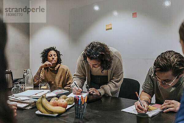 Männliche und weibliche Unternehmer schreiben in Notizblöcke  während sie bei einer Besprechung im Büro eine Strategie diskutieren