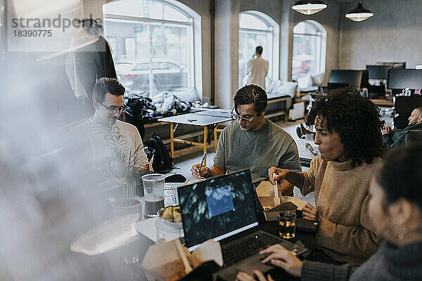 Geschäftsmann bei der Arbeit inmitten von männlichen und weiblichen Kollegen am Schreibtisch in einem kreativen Büro