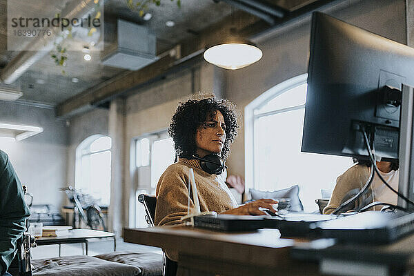 Weiblicher Hacker mit drahtlosen Kopfhörern um den Hals  der einen Computer bei der Arbeit im Büro benutzt