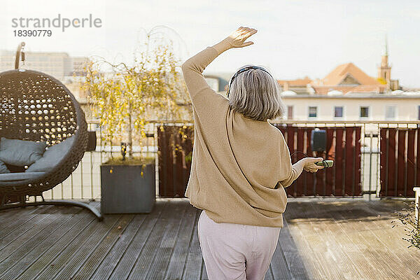 Rückansicht einer älteren Frau  die auf einer Terrasse tanzt und Musik hört