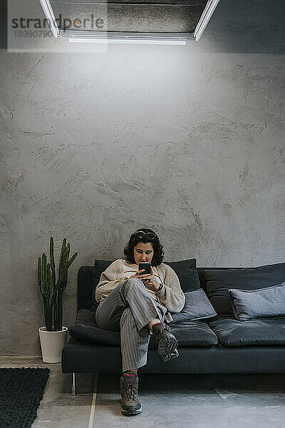 Junge Geschäftsfrau mit Smartphone auf dem Sofa im Kreativbüro
