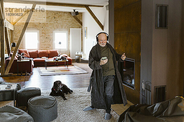 Sorgloser älterer Mann tanzt und hört Musik  während er zu Hause auf einem Teppich steht
