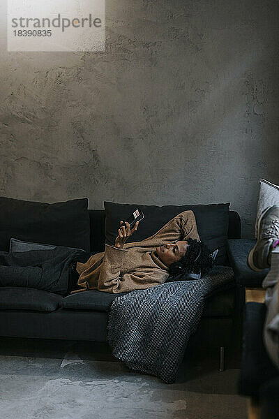 Geschäftsfrau  die ihr Smartphone benutzt  während sie sich auf dem Sofa im Kreativbüro ausruht