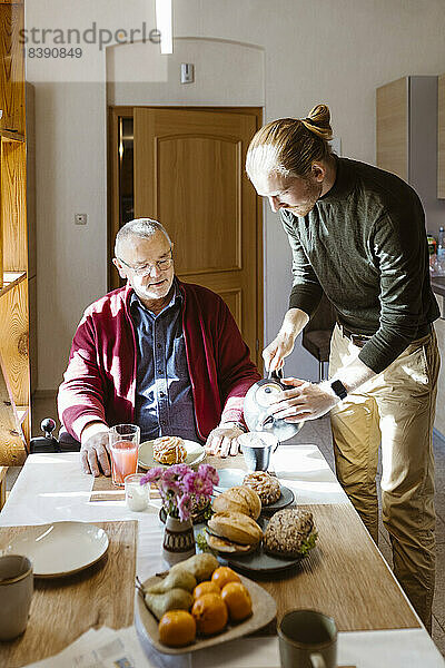Junger Mann schenkt seinem behinderten Vater im Ruhestand beim Frühstück zu Hause Kaffee ein