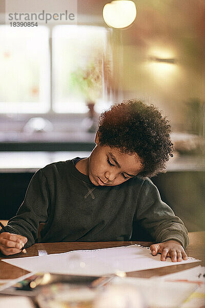 Junge mit lockigem Haar macht Hausaufgaben zu Hause