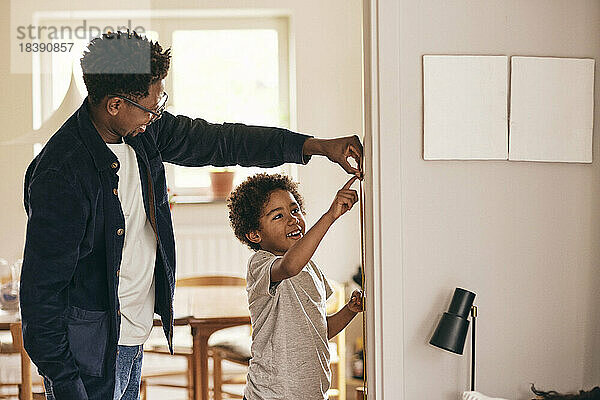 Glücklicher Vater und Sohn prüfen die Höhe  während sie zu Hause an der Wand stehen