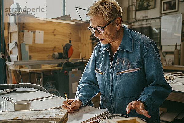 Älterer weiblicher Schreiner mit Brille bei der Vorbereitung eines Dokuments in der Werkstatt