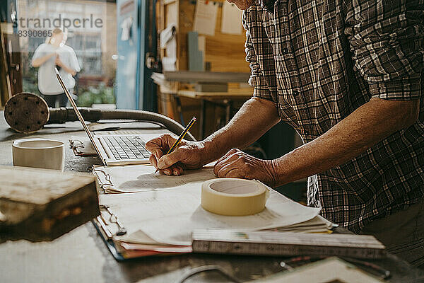 Mittelteil eines Handwerkers  der in einer Schreinerei mit einem Laptop ein Dokument vorbereitet