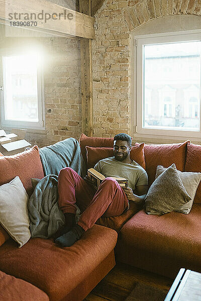 Junger Mann liest ein Buch und entspannt sich auf dem Sofa zu Hause