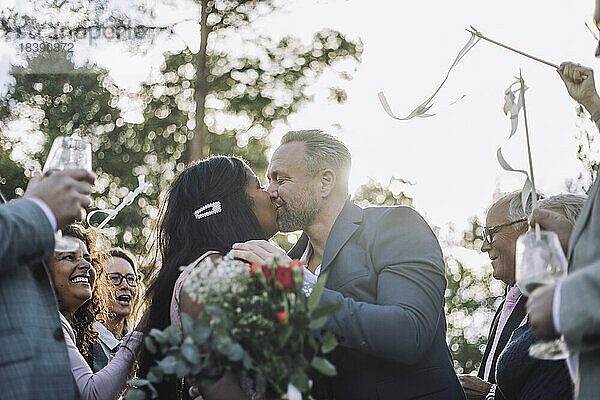Neuvermähltes Paar küsst sich auf den Mund  während die Gäste ihnen bei der Hochzeitszeremonie zujubeln