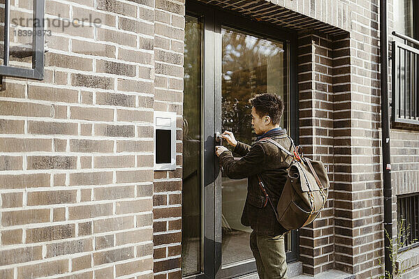 Mann entriegelt die Tür  während er vor der Wohnung steht