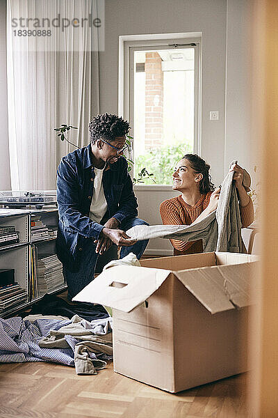 Ein Paar  das miteinander spricht  sortiert zu Hause Kleidung aus einem Karton