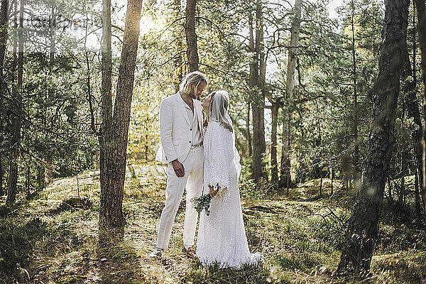 Die Braut schaut den Bräutigam an  während sie am Hochzeitstag inmitten von Bäumen im Wald steht