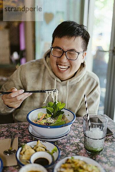Glücklicher junger Mann  der im Restaurant mit Stäbchen isst