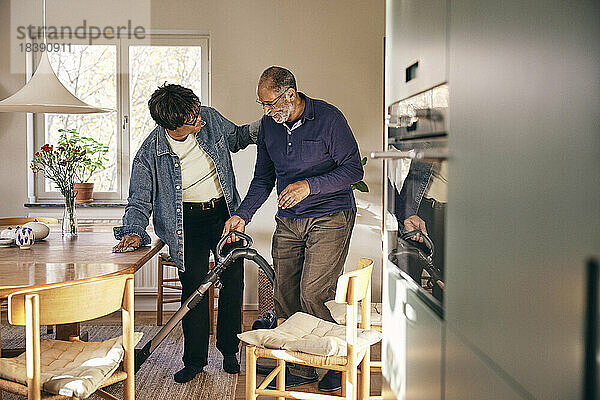 Ältere Frau im Gespräch mit einem Mann  der sein Haus mit einem Staubsauger reinigt