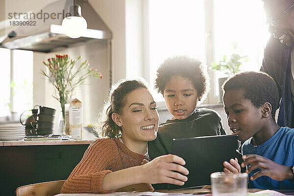 Lächelnde Mutter  die mit ihren Söhnen zu Hause ein digitales Tablet betrachtet