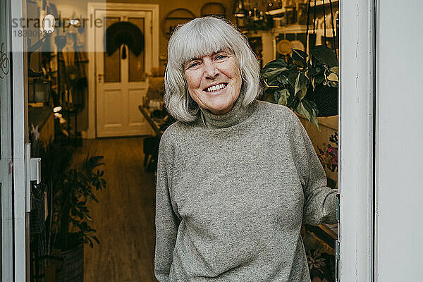 Porträt einer lächelnden Seniorin mit grauen Haaren am Ladeneingang