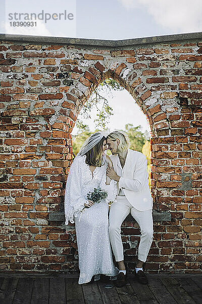 Lächelnder Bräutigam und lächelnde Braut sitzen sich auf der Fensterbank bei einer Hochzeit gegenüber