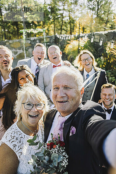 Fröhliches frisch verheiratetes älteres Paar  das ein Selfie mit Familie und Freunden bei der Hochzeit macht