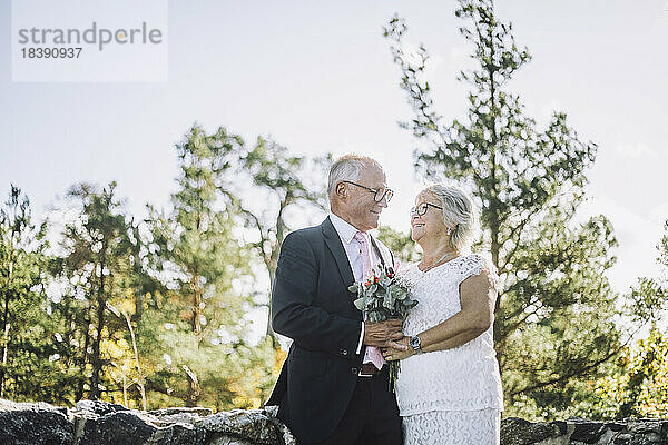 Lächelndes älteres Paar  das sich bei einer Hochzeit mit Blumenstrauß anschaut