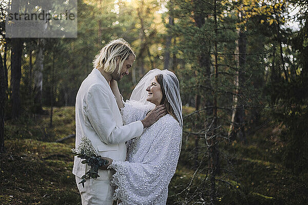 Lächelndes frisch verheiratetes Paar  das sich bei der Hochzeit im Wald ansieht