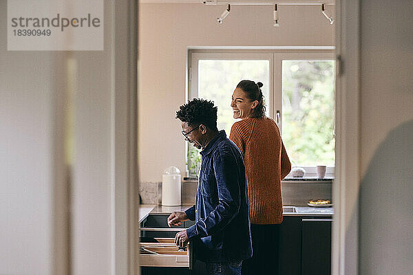 Glückliches gemischtrassiges Paar  das sich gegenseitig in der Küche zu Hause hilft