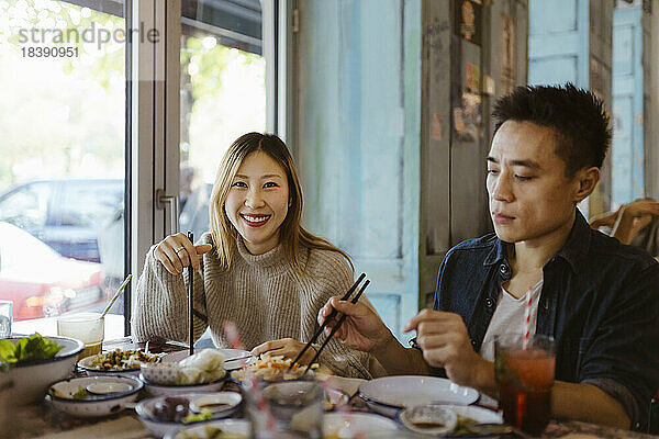 Porträt einer lächelnden Frau mit Stäbchen  die mit einem männlichen Freund im Restaurant isst