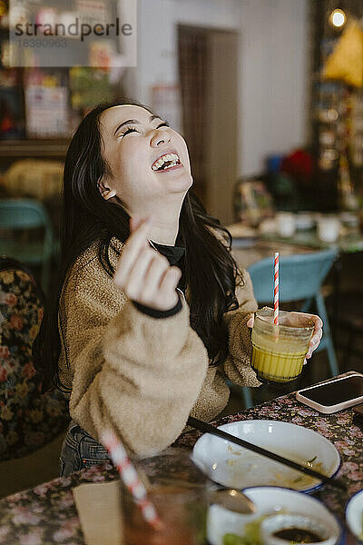 Junge Frau lacht und hält ein Getränk in einem Restaurant
