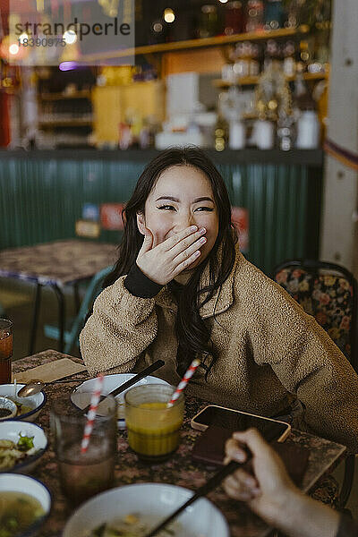 Lachende Frau mit zugehaltenem Mund im Restaurant