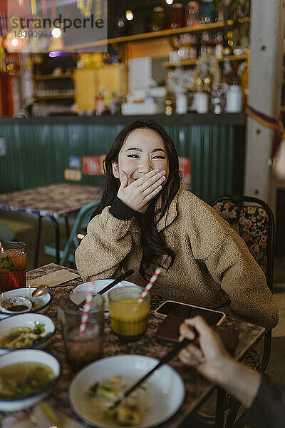 Porträt einer Frau  die den Mund bedeckt  während sie im Restaurant lacht