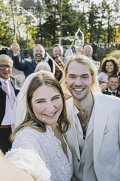 Porträt der glücklichen Braut  die ein Selfie mit dem Bräutigam und der Familie am Hochzeitstag macht