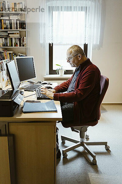Älterer Mann in voller Länge beim Tippen am Computer im Heimbüro