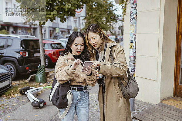 Junge Freundinnen teilen sich ein Smartphone  während sie auf dem Gehweg stehen